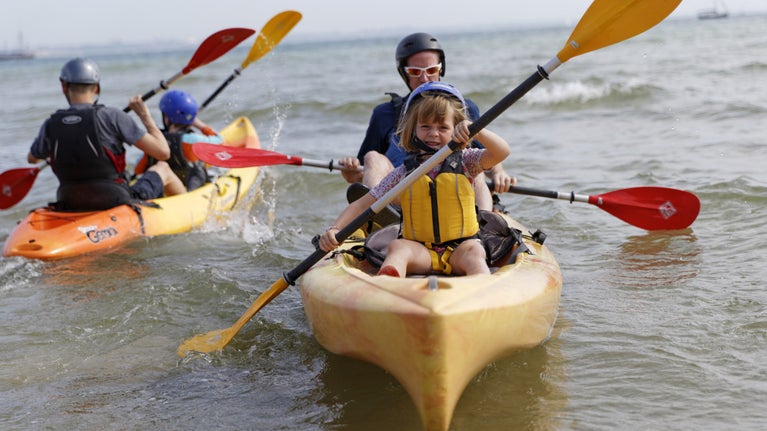 Two families kayaking on the sea in yellow and orange kayaks.
